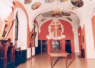 An ornate room with a long table, decorated ceiling, and religious frescoes.