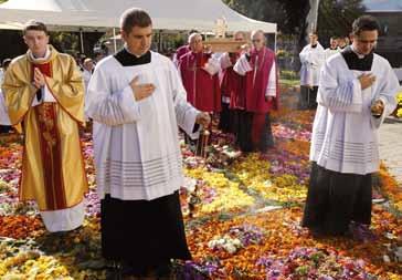 Clerics in ceremonial attire walking on a flower-covered path during a religious ceremony.