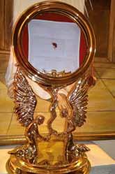 A golden monstrance displaying a small red relic, possibly a Eucharistic miracle.