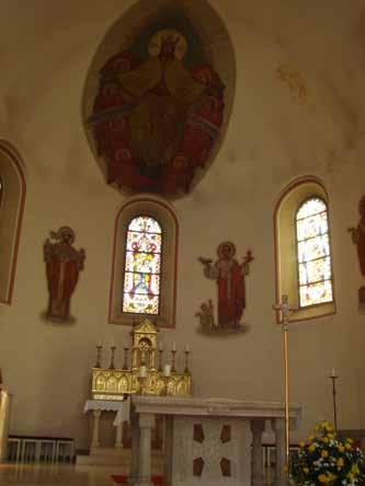 Interior of a church with an altar, stained glass windows, and religious artwork on the walls.
