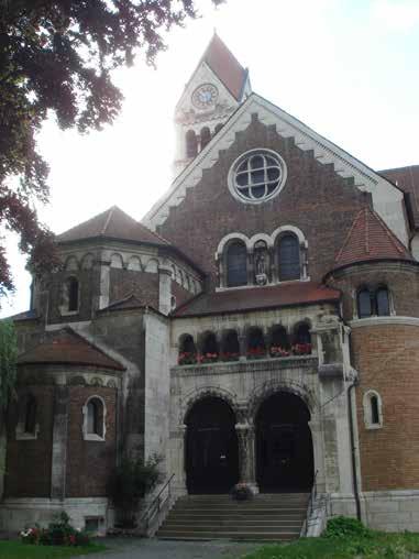 A brick church with arched windows and a clock tower, surrounded by trees.