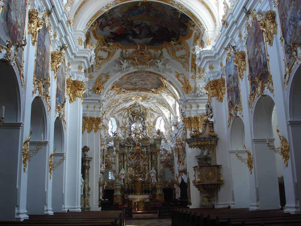Interior of a richly decorated church with ornate gold and white details and religious artwork.