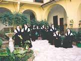 A group of nuns in black habits posing in a courtyard with plants.