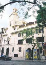 Image of the facade of a monastery with a tower and trees in front.