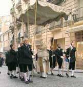A group of people in traditional attire carrying a canopy during a religious procession.