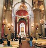 Interior view of a church with pews, chandeliers, and people attending a service.