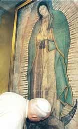 A person kneeling before the image of the Virgin of Guadalupe in a religious setting.