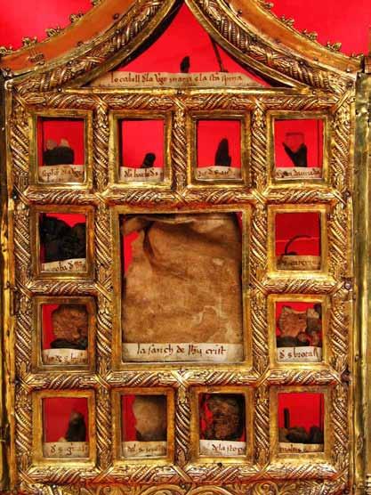 An ornate reliquary with multiple compartments displaying relics against a red background.
