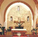 An altar with a crucifix and floral arrangements in a stone-walled church interior.