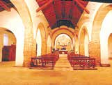 Interior view of a church with stone arches and wooden pews leading to an altar.
