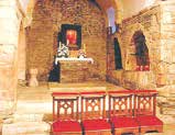 An altar with stone walls and wooden benches in a historic church setting.