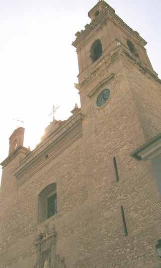 A tall church tower with a clock and cross on top, made of stone.