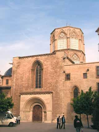 A historic church building with a distinctive tower and entrance, surrounded by trees and people.