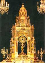 A golden altar with a monstrance, surrounded by ornate chandeliers.