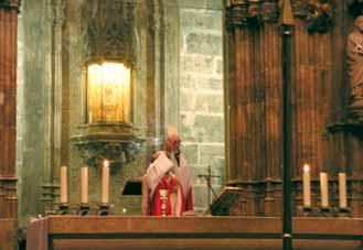 A priest performing a mass in front of an altar with candles and a lit tabernacle.